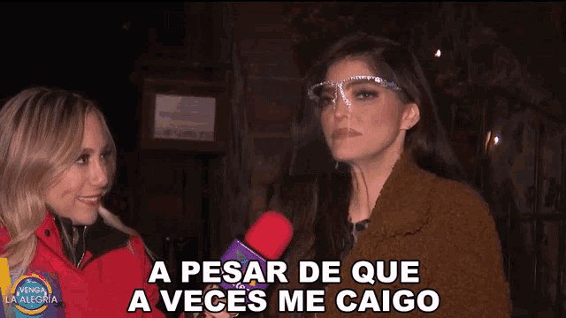 a woman wearing a face shield talks into a microphone while another woman says a pesar de que