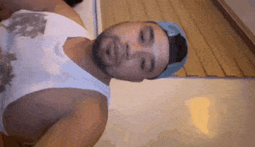a man wearing a white tank top and a blue hat looks down