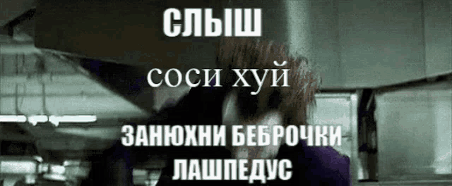 a man in a purple jacket is standing in front of a sign that says ' coci хуй ' on it .