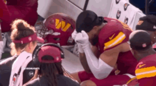 a football player is kneeling down in a huddle with his hands on his head .
