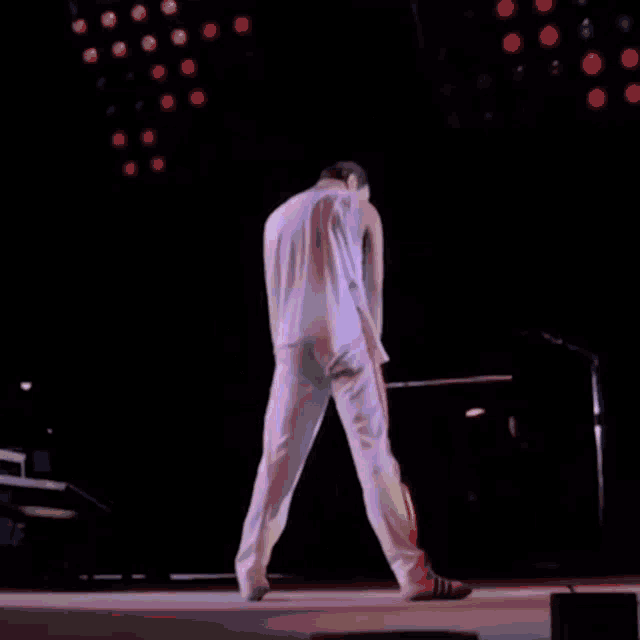 a man in a white tank top and white pants is dancing on a stage in front of a microphone .