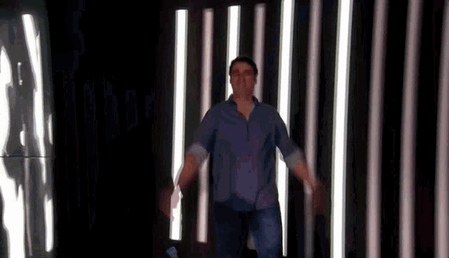 a man in a blue shirt is dancing in front of a wall of lights