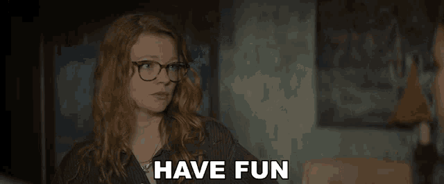 a woman wearing glasses says " have fun " in a dark room