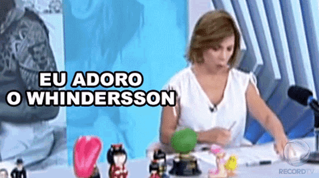 a woman is sitting at a table with a microphone and the words eu adoro o whindersson above her