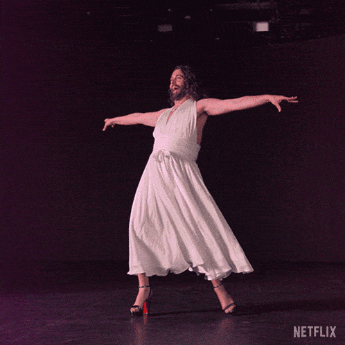 a man in a white dress and high heels is dancing on a stage with a netflix logo in the background
