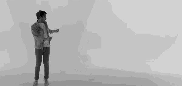a man is dancing in a black and white photo in front of a white wall .