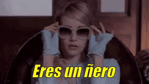 a woman wearing sunglasses and gloves is sitting in a chair and says " eres un hero "