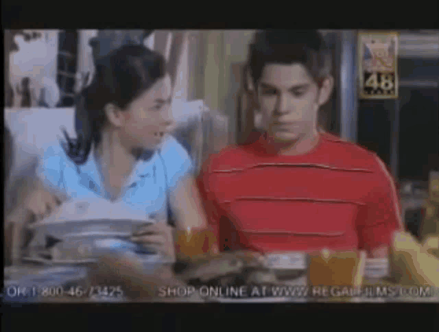 a man and a woman are sitting at a table and the man is wearing a red shirt