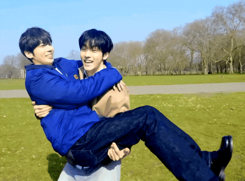 a man is carrying another man in his arms in a park