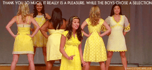 a group of women in yellow dresses are standing on a stage and one of them is pointing