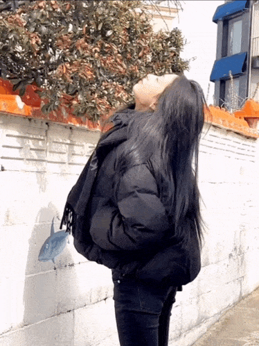 a woman in a black jacket stands in front of a brick wall