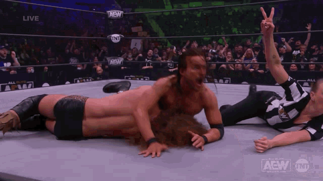 a wrestler is laying on the ground while a referee gives a peace sign