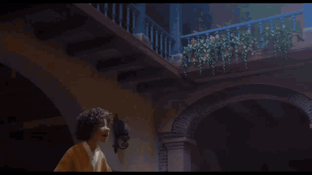 a man stands in front of a balcony with potted plants hanging from it
