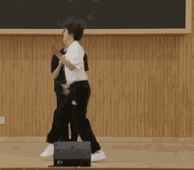 two people are hugging each other in front of a wooden wall and a blackboard