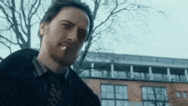 a man is smoking a cigarette in front of a building and trees .