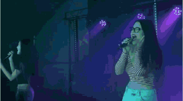 a woman singing into a microphone in front of a purple light