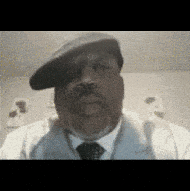 a man wearing a beret and a vest looks at the camera
