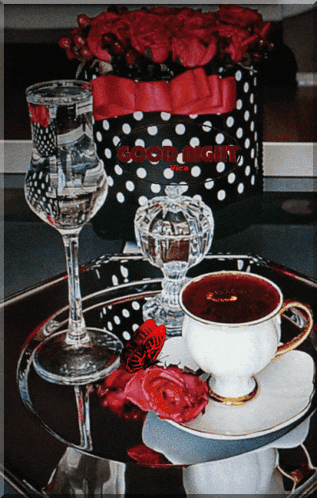 a cup of coffee sits on a saucer next to a glass of water and a box of roses