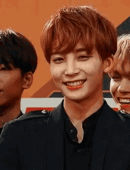 a young man with red hair is smiling for the camera while standing next to another young man .