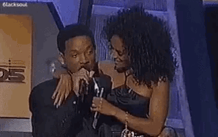 a man and a woman are standing next to each other in front of a microphone at a awards show .