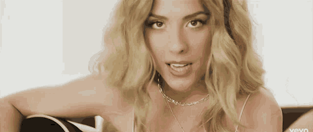 a woman with blonde hair is holding a guitar and wearing a necklace that says ' vevo ' on it