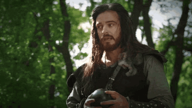 a man with long hair and a beard is holding a skull in his hands
