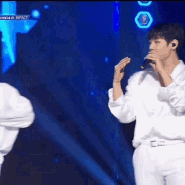 two men are singing into microphones on a stage in front of a blue light .