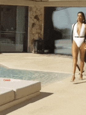 a woman in a white swimsuit walks by a pool