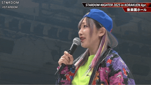a woman in a blue hat is holding a microphone in front of a sign that says stardom