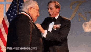 a man in a tuxedo is putting a medal around another man 's neck and the words wearechange.org are visible