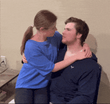 a woman in a blue shirt is hugging a man in a black hoodie