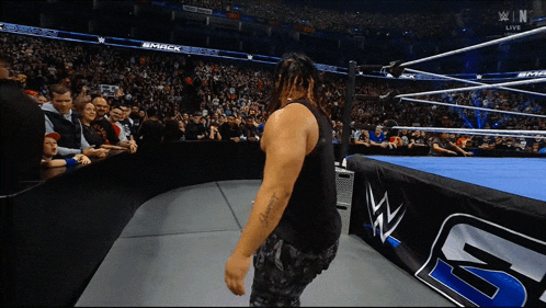 a man in a black tank top stands in a wrestling ring with a banner that says smack on it