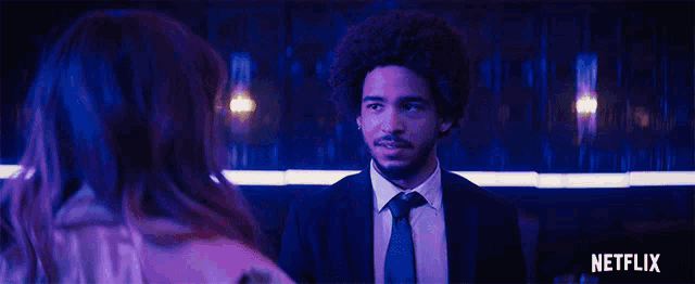 a man in a suit and tie is talking to a woman in a dark room with a netflix logo in the corner