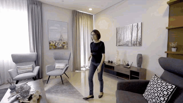 a woman is standing in a living room with chairs and a painting on the wall