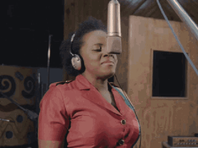 a woman wearing headphones sings into a microphone in a recording studio