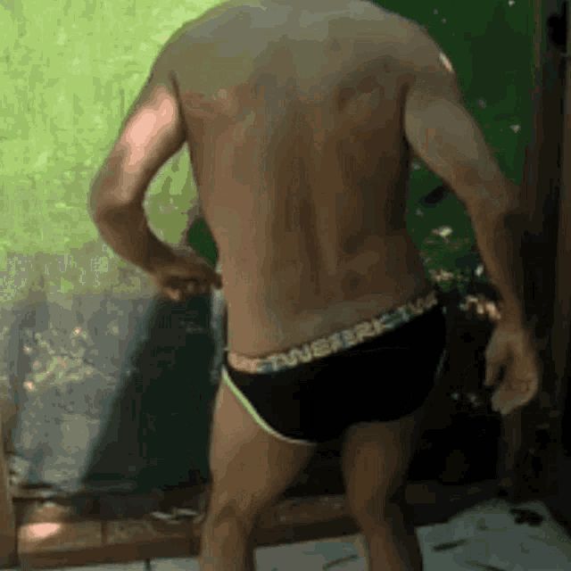 a shirtless man in black underwear is standing in front of a green curtain .
