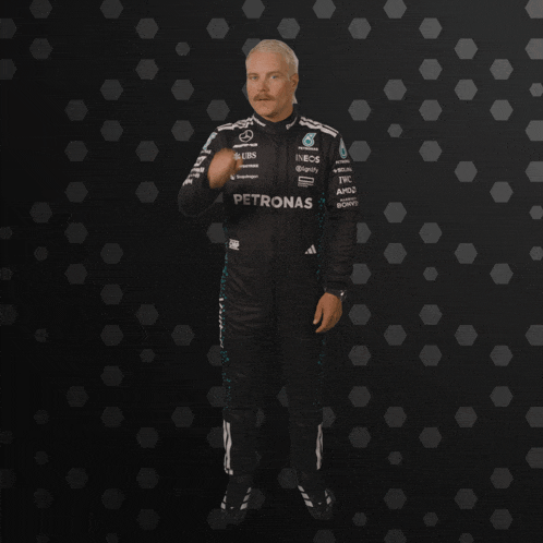 a man wearing a petronas racing suit stands in front of a black background