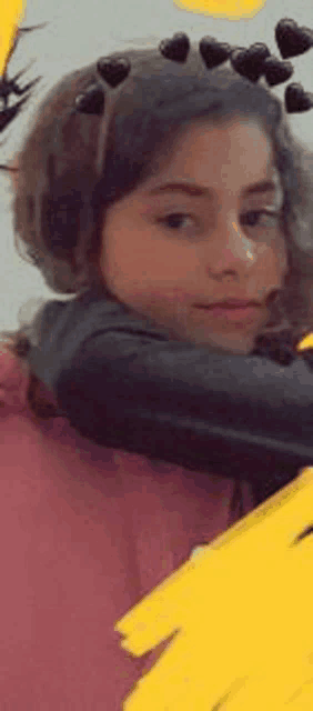 a young girl wearing a headband with hearts on it is hugging someone .