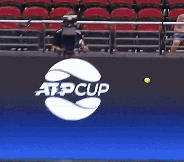 a tennis player serves a ball in front of a sign that says atpcup