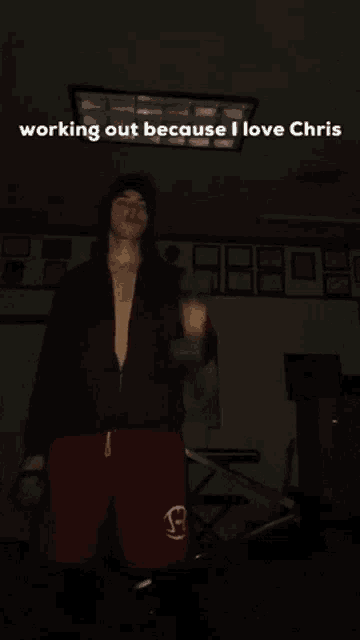 a man in a black jacket and red shorts is standing in a dark room with the words working out because i love chris above him