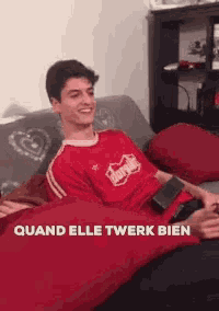 a man in a red shirt is sitting on a couch with the words " quand elle twerk bien " below him