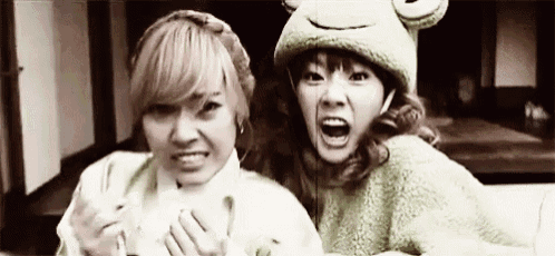 two women are making funny faces together and one of them is wearing a frog hat .