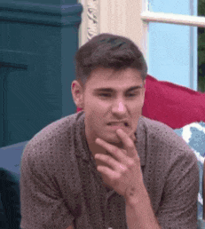 a young man is sitting on a couch with his hand on his chin and making a funny face .