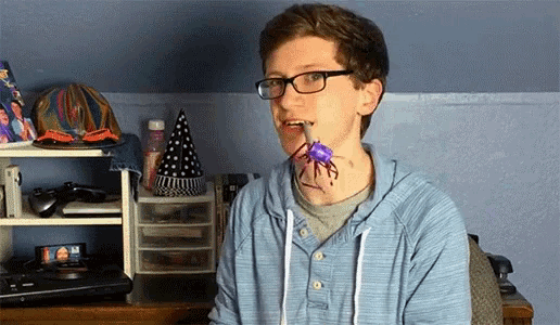 a boy wearing glasses holds a toy crab in his mouth