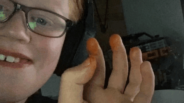 a man wearing glasses and headphones is holding a small orange object in his hand