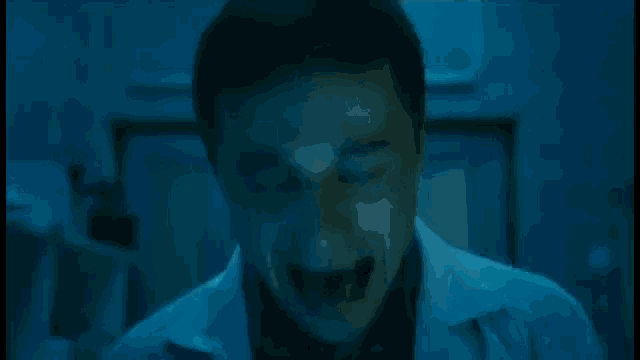 a man in a lab coat is screaming with his mouth wide open in a dark room .