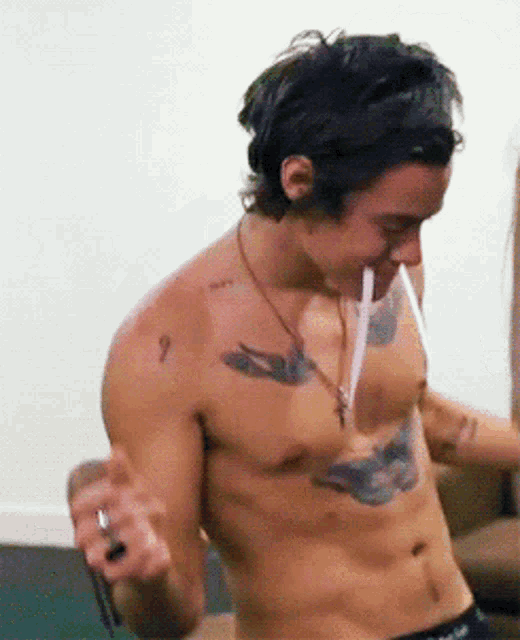 a shirtless man with a tattoo of a bird on his chest is smoking a cigarette with a straw