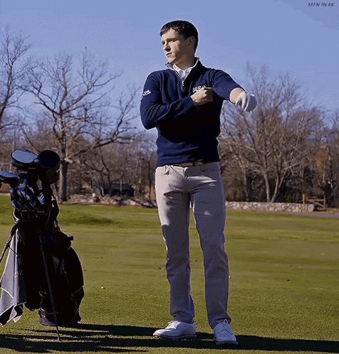 a man is standing on a golf course with a bag of golf clubs in the background