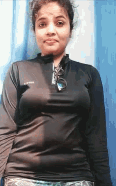 a woman in a black shirt is standing in front of a blue curtain and making a funny face .