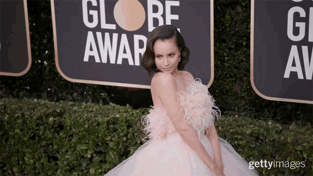 a woman in a pink dress stands in front of a sign that says globe award